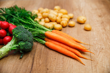 Potatoes with carrot. Red radish, brocoli and raw new potato. Fresh natural vegetables. Organic bio food. On wooden table.