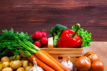 Vegetables. Potatoes, carrot and red pepper. Lettuce salad, garlic and brocoli. Onion and radish. Wooden basket on rustic table.