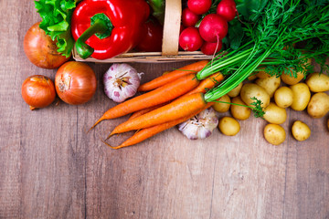 Vegetables. Potatoes, carrot and red pepper. Lettuce salad, garlic and brocoli. Onion and radish. Wooden basket on rustic table.