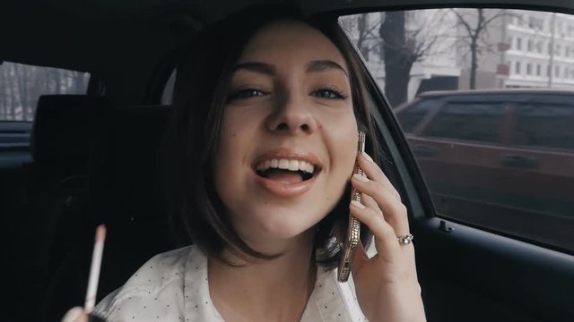 Young woman doing make-up in car and speaking phone