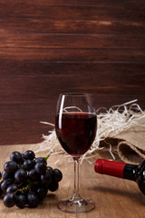 Red wine. Bottle and Wineglass with dark grapes branch. On rustic wooden background.