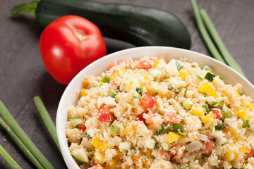 Tabbouleh salad with couscous, tomatoes, onion, zucchini and bell peppers topped with basil leaf angled shot