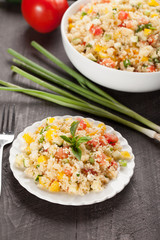 Tabbouleh salad with couscous, tomatoes, onion, zucchini and bell peppers topped with basil leaf vertical shot