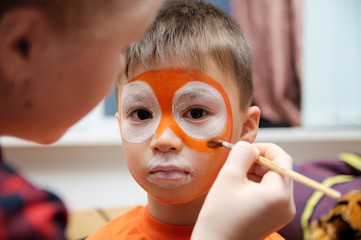Make up artist making tiger mask for child.Children face painting. Boy painted as tiger or ferocious lion. Preparing for theatrical performance. Boy actor playing role. Tiger mask face