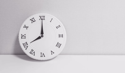 Closeup white clock for decorate in 8 o'clock on white wood desk and wallpaper textured background in black and white tone with copy space