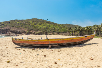 Obraz premium Wide view of a fishing boat parked alone in seashore with mountain in the background, Visakhapatnam, Andhra Pradesh, March 05 2017