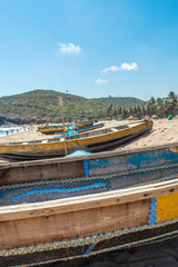 Wide view of group of fishing boats parked alone in seashore with people in the background, Visakhapatnam, Andhra Pradesh, March 05 2017