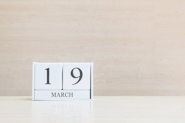 Closeup surface white wooden calendar with black 19 march word on blurred brown wood desk and wood wall textured background with copy space , selective focus at the calendar