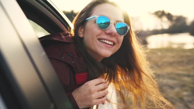 Happy young woman sitting in car passenger seat and looking out window on sunny day