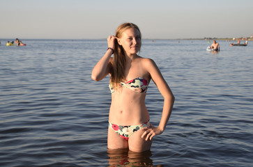 Blond girl in a bikini standing in the sea water. Beautiful young woman in a colorful bikini on sea background