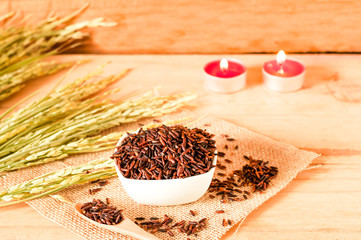 the brown raw rice in bowl with  dried rice plant on wooden table background.