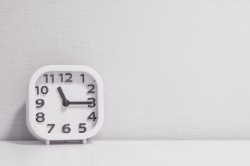 Closeup white clock for decorate show a quarter past eleven or 11:15 a.m. on white wood desk and cream wallpaper textured background in black and white tone with copy space