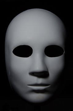 White mask with neutral expression and shadows on dark background