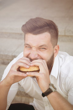 City hipster businessman eating hamburger. Close-up portrait of hungry man having a snack during his break after hard work. Toned image.