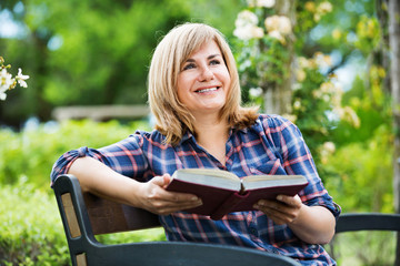 Portrait of  woman sitting on bench and reading book in garden