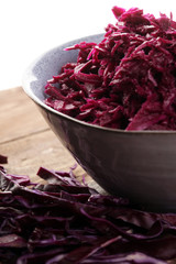 Shredded red cabbage in clay bowl on wooden background. Vegetari