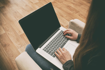 Fototapeta premium The young woman is sitting on the sofa and working at laptop
