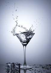 Splash from ice cube in martini glass isolated