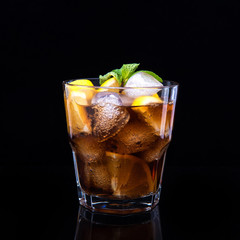 Glass of cola with ice, mint and lemon on black background
