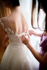 Obraz na płótnie Canvas Woman in violet dress laces up bride's corset