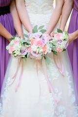 Obraz na płótnie Canvas Bride and bridesmaids in violet dresses hold together tender wedding bouquets
