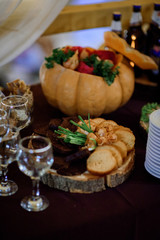 Wooden plate with cheese and bread stands on dinner table covered with dark cloth