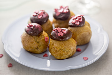 Choux pastry profiteroles with mousse topped with chocolate decorated with heart shaped candies