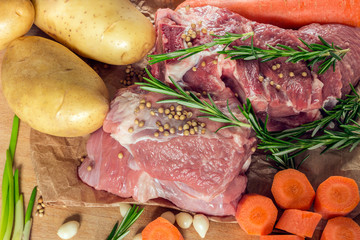 Raw meat with vegetables and greens on a wooden table surface.