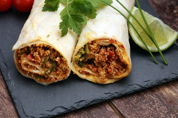 Delicious homemade vegetarian couscous wrap with tomatoes, carrots, zucchini, yellow bell pepper and fresh basil on a dark rustic wooden kitchen table