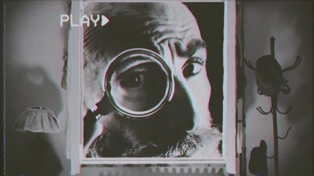 Fake VHS tape: an old man looking into a dolls' house with a magnifying glass. Black and white vintage close-up shot.
