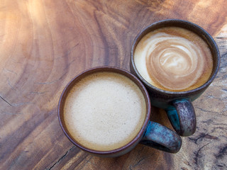 Two cups of hot coffee cappuccino on wood texture background in morning sunlight.