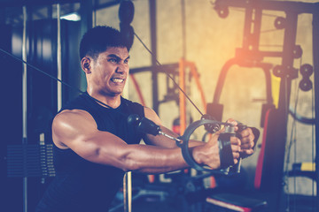 Handsome muscular man exercise with cable weight machine in gym.