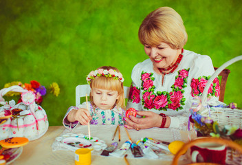 Fototapeta premium Granny helps her granddaughter to paint Easter eggs