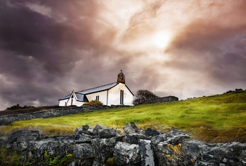 Small white chruch with cross and bell in dramatic cloudy sky