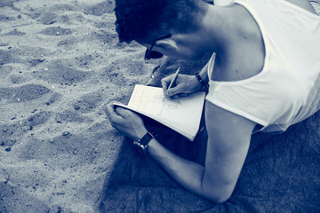 man writing his diary on the beach