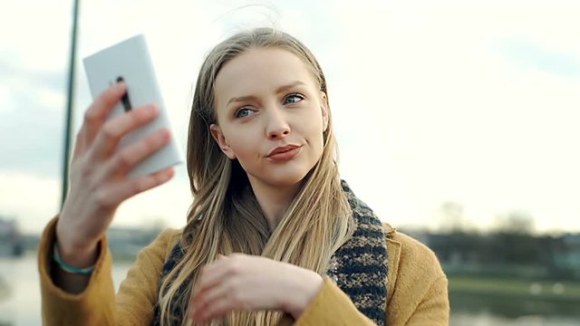 Pretty, blonde girl using smartphone as a mirror while checking her appearance
