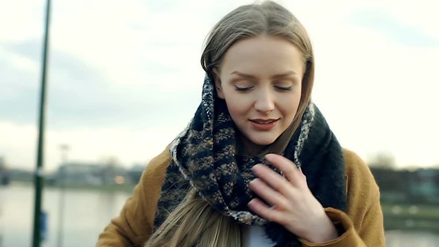 Girl looks cold while standing next to the river and wrap herself up
