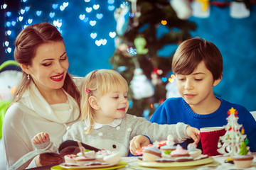 Smiling little boy sits with his mother and sister at dinner table in room with Christmas tree