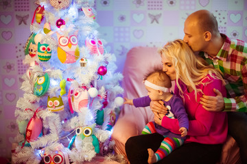 Man hugs his woman tender while they sit with daughter before Christmas tree