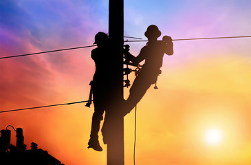 Silhouette two electrical engineer on electricity pole, work on electric post power pole and repair...