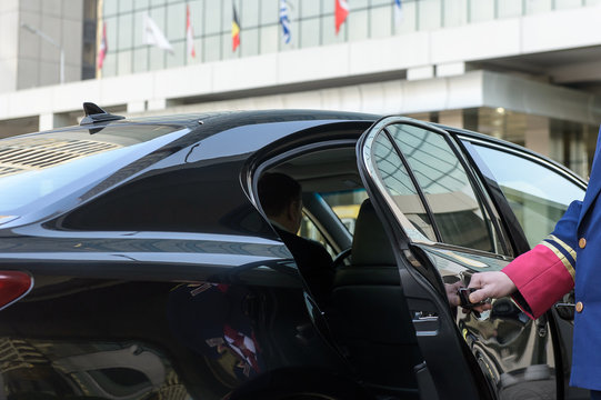 the doorman opens the door of a luxury car