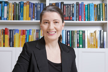 Friendly smiling mature woman in an office with lots of books, professor, teacher, lawyer, manager,...