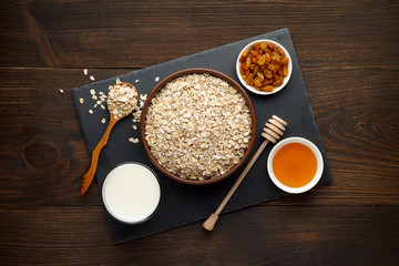 Healthy breakfast on rustic wooden background. Oat flakes with milk, honey and raisins on slate board.