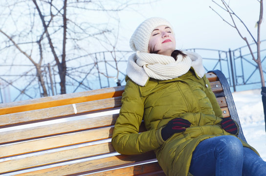 Young woman sitting on a bench and relaxing in sunny winter day. 