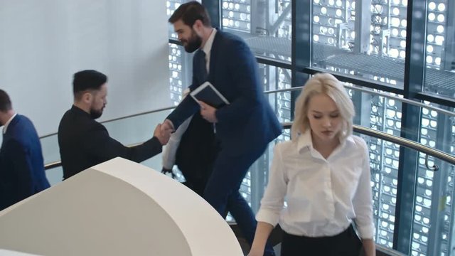 Busy businesspeople coming up and down spiral staircase in modern building 