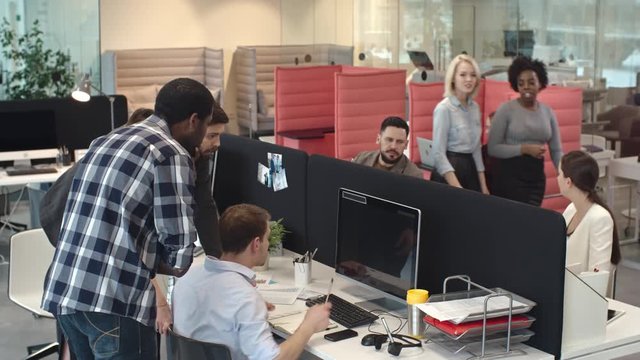 Team of businesspeople standing in busy office and looking over shoulder of frustrated male colleague working on computer: they discussing problem and trying to find solution 