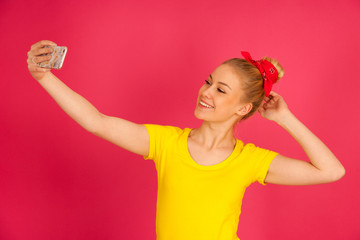 Beautiful young blond teenage woman in yellow t shirt  taking selfie over pink background.
