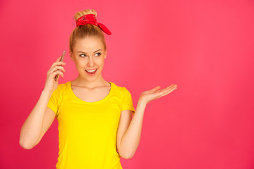 cut teenage woman in yellow t shirt talks on smart phone  over pink bacckground