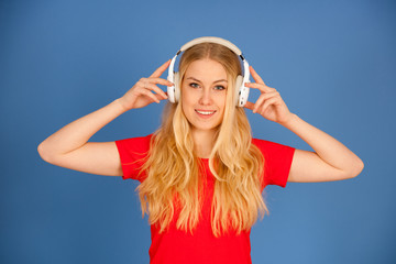 Young blonde woman with headphones  listens to the music over blue background