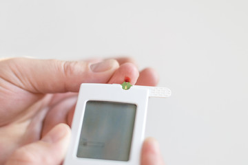 Medicine, diabetes, glycemia, health care and people concept - Close up of man hands testing high blood sugar level with glucometer or glucose meter and test stripe at home